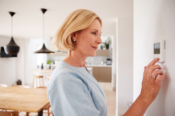 Homeowner Adjusting Thermostat At Home For Summer